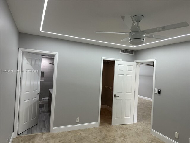 unfurnished bedroom featuring a closet, a spacious closet, ensuite bath, and ceiling fan