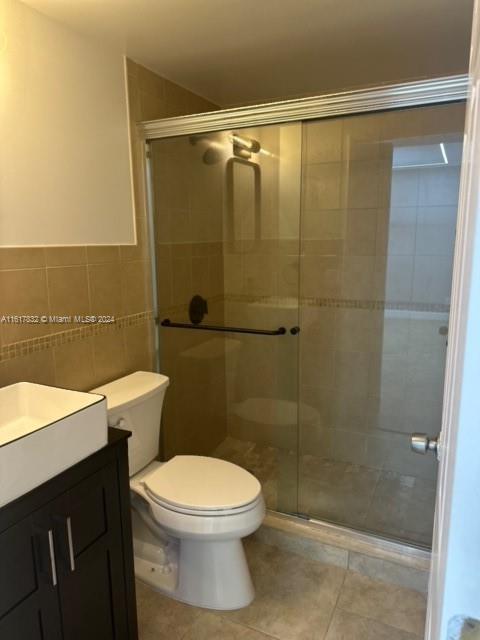 bathroom featuring walk in shower, vanity, tile walls, tile patterned flooring, and toilet