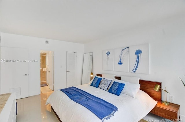 bedroom featuring light tile patterned floors, visible vents, and ensuite bath