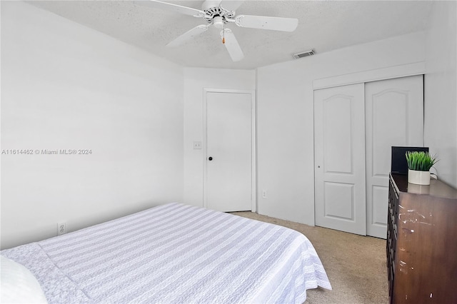 bedroom featuring ceiling fan, a closet, light colored carpet, and a textured ceiling