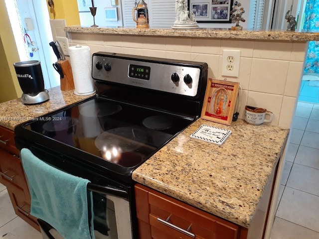 kitchen with backsplash, black range with electric stovetop, and light stone counters