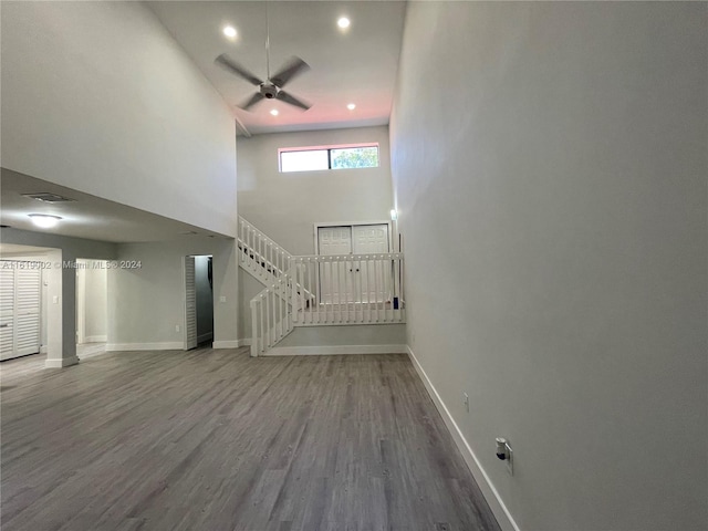 unfurnished living room with wood-type flooring, ceiling fan, and a high ceiling