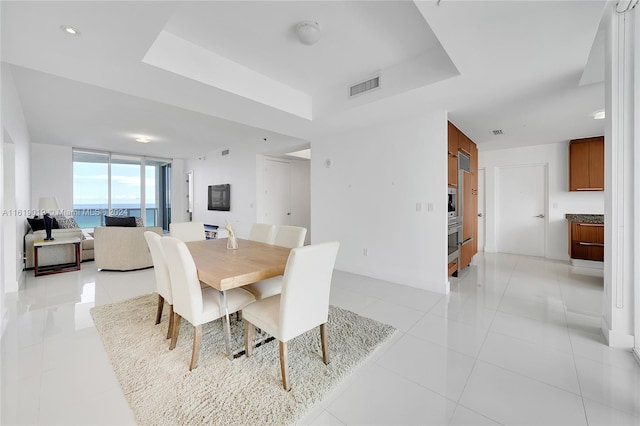 tiled dining room featuring a raised ceiling and a water view