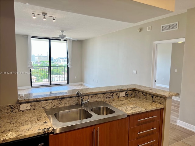 kitchen featuring ceiling fan, sink, kitchen peninsula, a textured ceiling, and light wood-type flooring