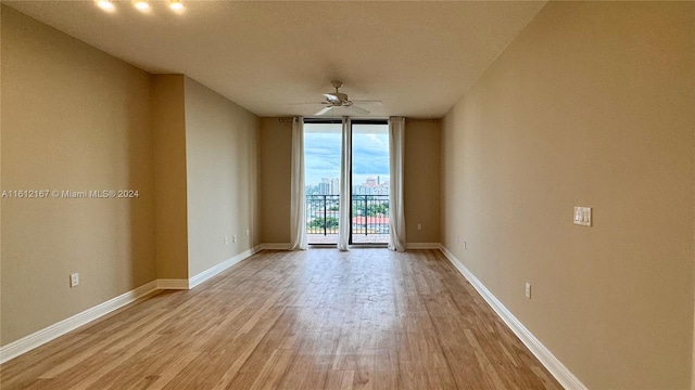 spare room with a wall of windows, light hardwood / wood-style floors, and ceiling fan