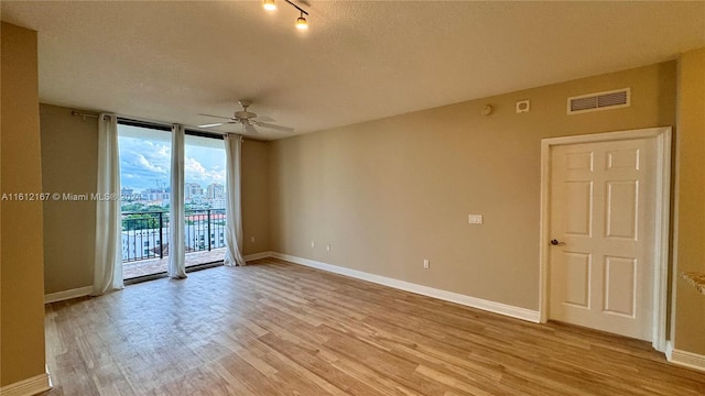 unfurnished room featuring ceiling fan, a wall of windows, light hardwood / wood-style flooring, and a textured ceiling