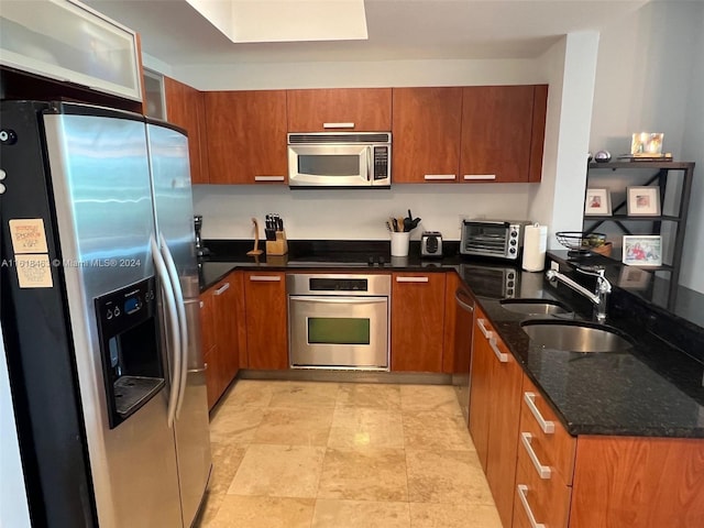 kitchen with appliances with stainless steel finishes, dark stone counters, and sink