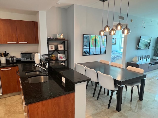 kitchen featuring sink, dark stone counters, pendant lighting, a breakfast bar area, and a kitchen island