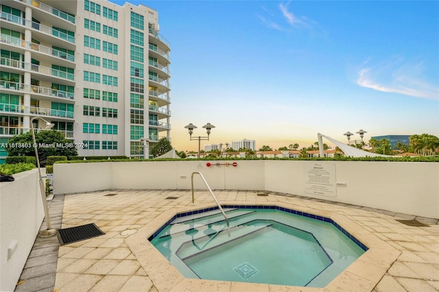 pool at dusk with a hot tub and a patio area