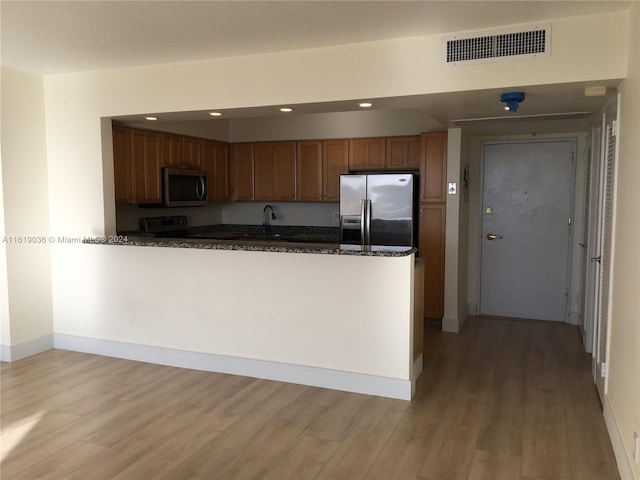 kitchen with sink, light hardwood / wood-style flooring, dark stone countertops, appliances with stainless steel finishes, and kitchen peninsula