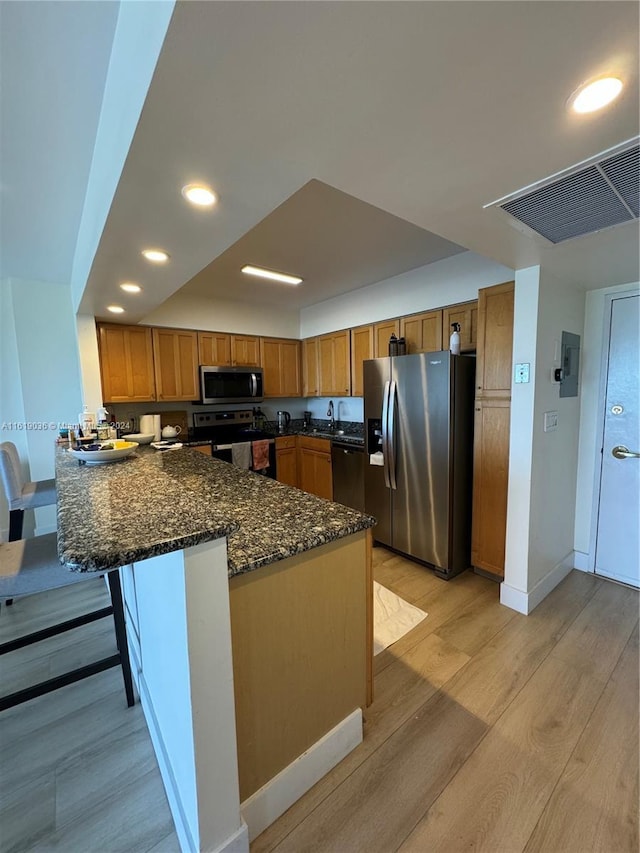 kitchen with appliances with stainless steel finishes, sink, dark stone countertops, kitchen peninsula, and light hardwood / wood-style flooring