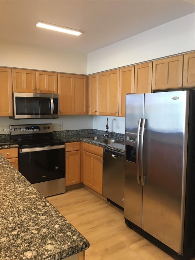 kitchen with appliances with stainless steel finishes, light hardwood / wood-style floors, sink, and dark stone countertops