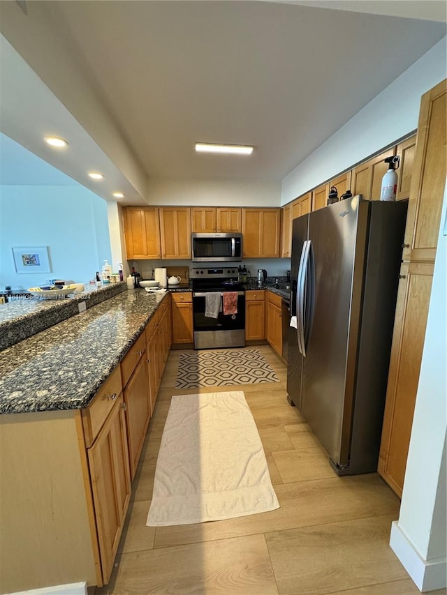 kitchen featuring appliances with stainless steel finishes, light hardwood / wood-style flooring, and dark stone counters