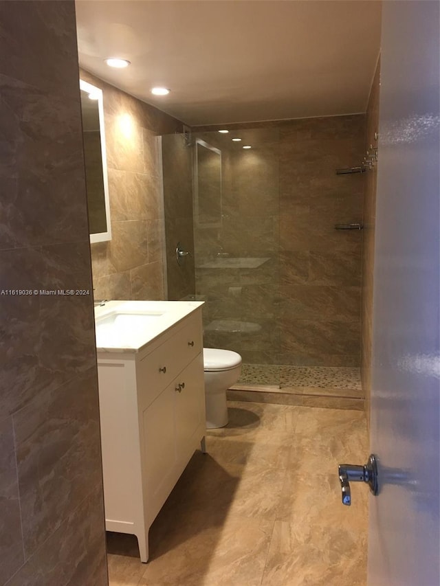 bathroom with vanity, tiled shower, tile walls, and toilet