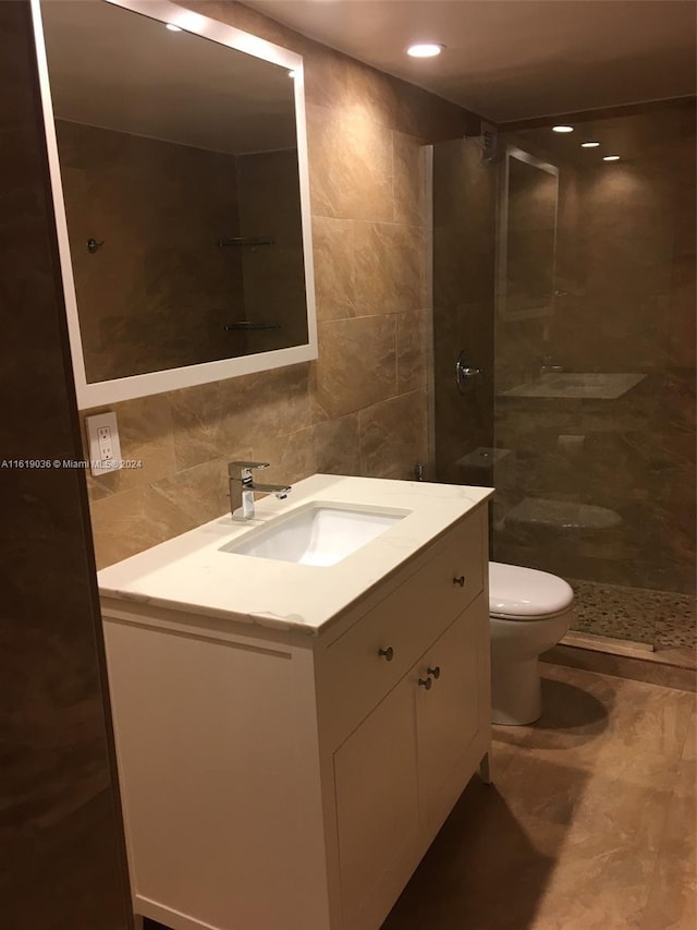 bathroom featuring vanity, toilet, tile walls, and a tile shower