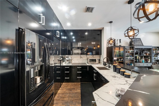 kitchen with light stone countertops, hanging light fixtures, sink, decorative backsplash, and black fridge