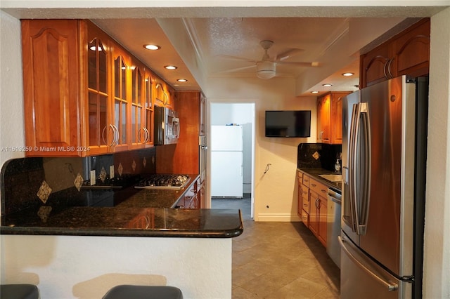 kitchen with a breakfast bar area, appliances with stainless steel finishes, kitchen peninsula, ceiling fan, and decorative backsplash