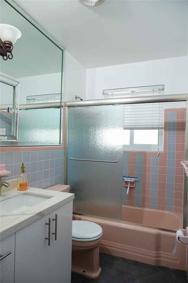 full bathroom with tile walls, tile patterned flooring, bath / shower combo with glass door, vanity, and toilet