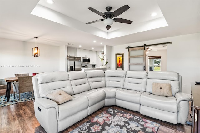 living room with dark wood-type flooring, a tray ceiling, and ceiling fan