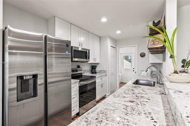 kitchen featuring white cabinetry, dark wood-type flooring, light stone counters, appliances with stainless steel finishes, and sink