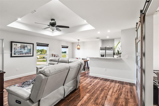 living room featuring dark hardwood / wood-style flooring, a barn door, ceiling fan, and a tray ceiling