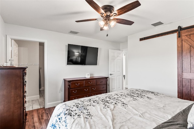 bedroom with dark wood-type flooring, connected bathroom, a barn door, and ceiling fan