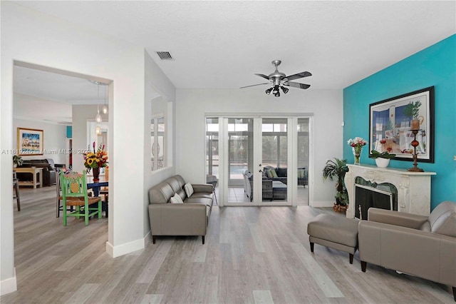 living room with light hardwood / wood-style floors, a fireplace, ceiling fan, and french doors