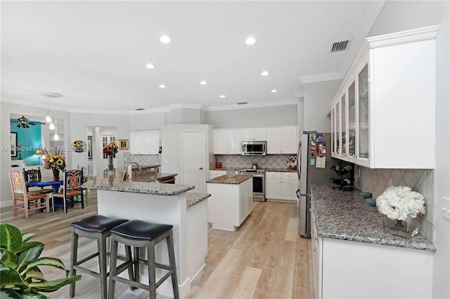 kitchen featuring light hardwood / wood-style floors, a kitchen island with sink, white cabinetry, decorative backsplash, and appliances with stainless steel finishes