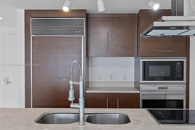 kitchen featuring black microwave, stovetop, wall chimney range hood, sink, and stainless steel oven