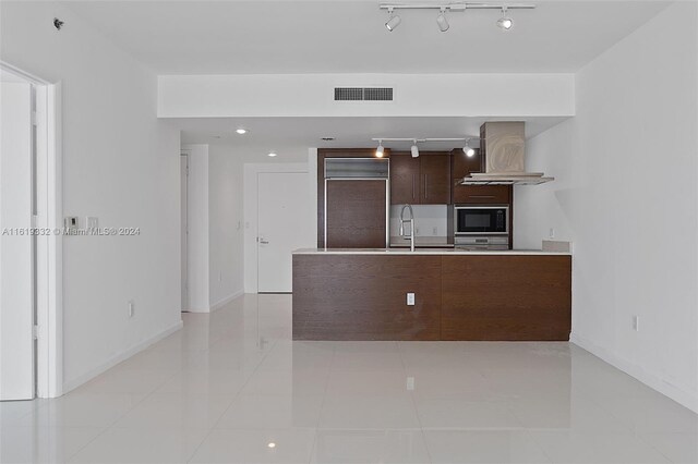 kitchen featuring light tile patterned floors, wall chimney range hood, black microwave, track lighting, and sink