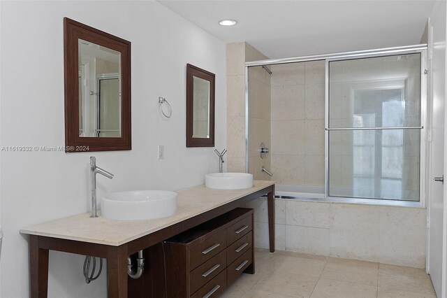 bathroom with combined bath / shower with glass door, dual bowl vanity, and tile patterned floors