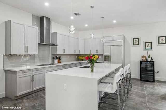 kitchen featuring wall chimney exhaust hood, beverage cooler, decorative light fixtures, a kitchen bar, and a center island with sink