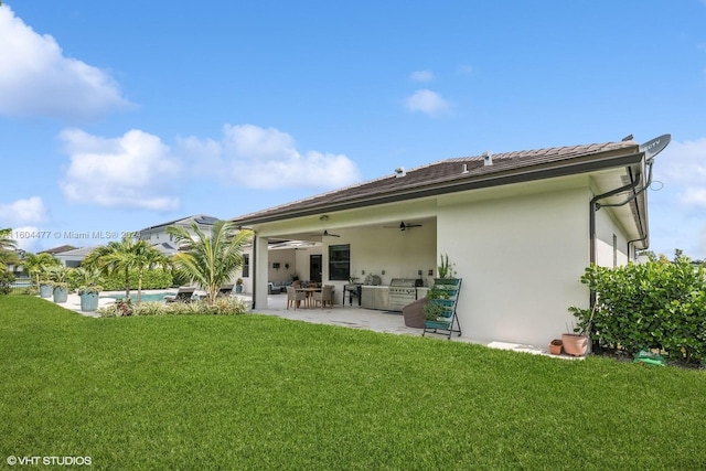 rear view of property with a yard, an outdoor kitchen, ceiling fan, and a patio area