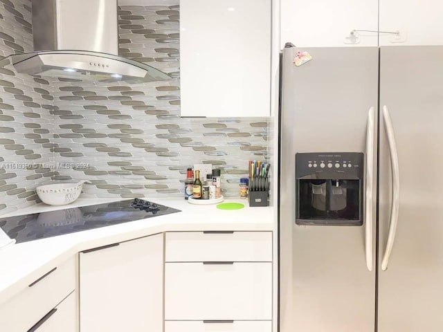 kitchen featuring decorative backsplash, stainless steel refrigerator with ice dispenser, wall chimney range hood, stovetop, and white cabinetry