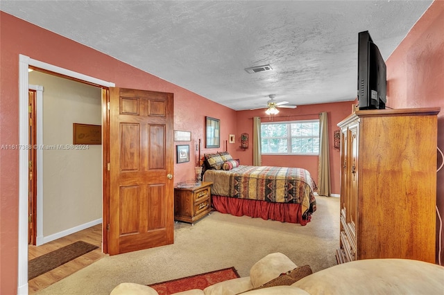 bedroom with light colored carpet, a textured ceiling, and ceiling fan