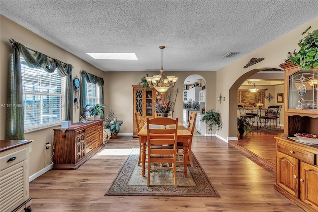 dining area featuring light wood-type flooring, a textured ceiling, a skylight, and an inviting chandelier