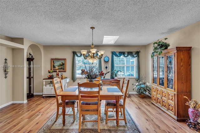 dining space featuring a textured ceiling, a skylight, an inviting chandelier, and light hardwood / wood-style floors