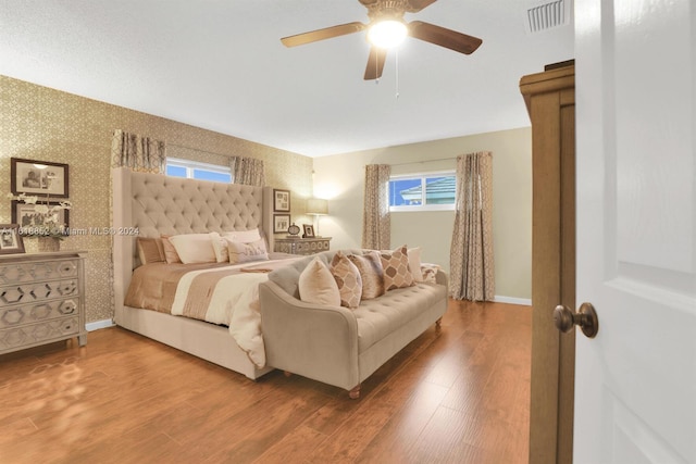 bedroom with baseboards, wood finished floors, visible vents, and wallpapered walls