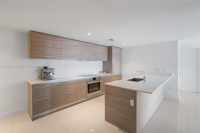 kitchen featuring light tile patterned flooring, black electric cooktop, stainless steel oven, kitchen peninsula, and sink