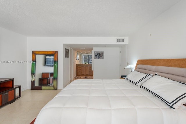 bedroom featuring ensuite bath, a textured ceiling, and light tile patterned floors