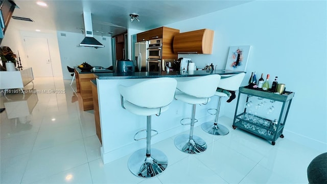 kitchen with kitchen peninsula, light tile patterned floors, stainless steel appliances, and a breakfast bar area