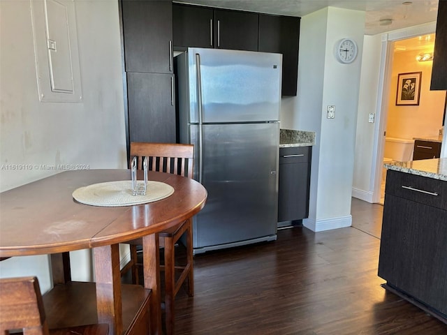 kitchen with electric panel, dark hardwood / wood-style floors, light stone counters, and stainless steel refrigerator