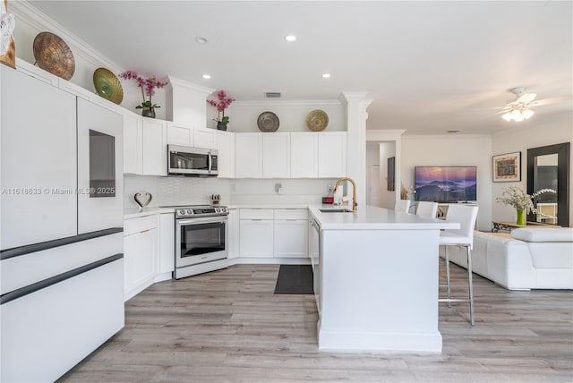 kitchen featuring stainless steel appliances, a peninsula, a sink, open floor plan, and a kitchen bar