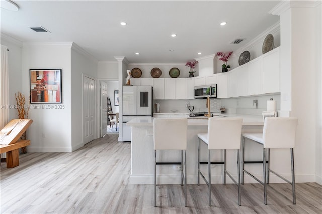 kitchen featuring visible vents, stainless steel microwave, a peninsula, light countertops, and backsplash