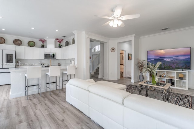 living room featuring ornamental molding, stairway, visible vents, and light wood-style flooring