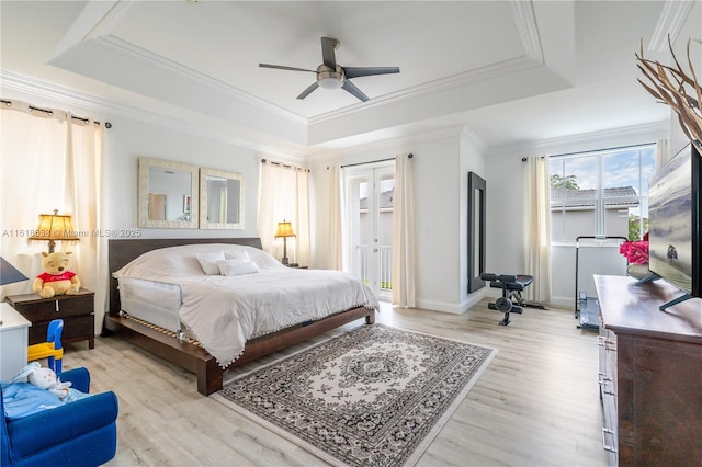 bedroom featuring light wood finished floors, baseboards, a tray ceiling, and crown molding