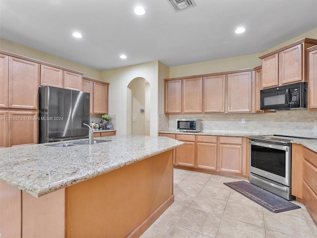 kitchen featuring light brown cabinetry, light stone countertops, sink, stainless steel appliances, and a center island with sink