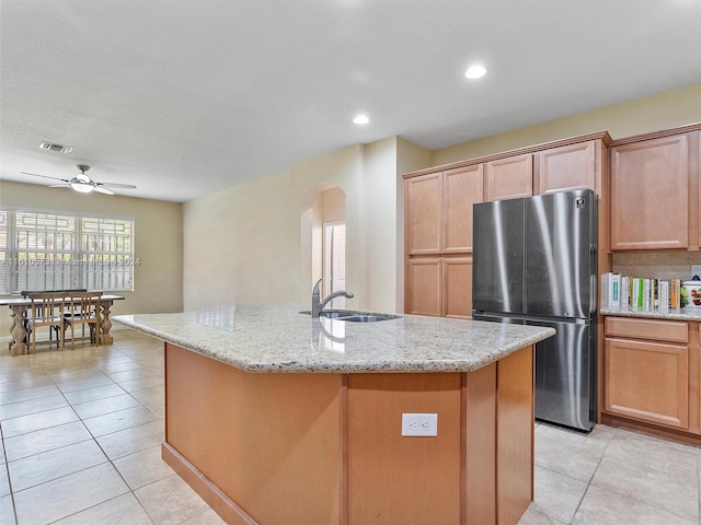 kitchen featuring an island with sink, sink, light tile patterned floors, and stainless steel refrigerator