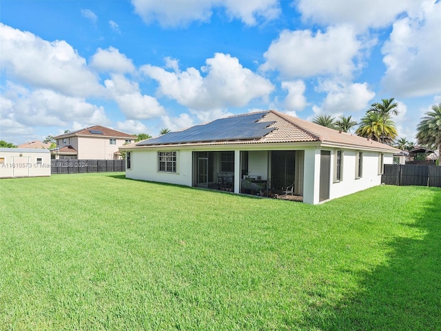 back of house featuring a sunroom, a lawn, and solar panels