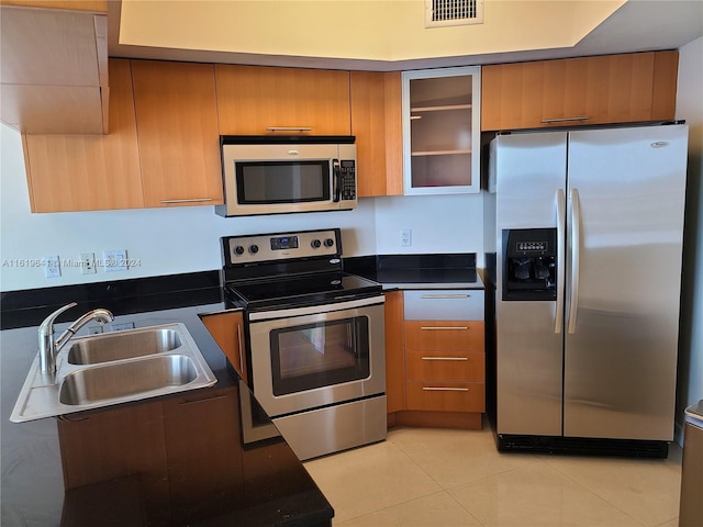 kitchen featuring sink, dark stone countertops, light tile patterned floors, and appliances with stainless steel finishes